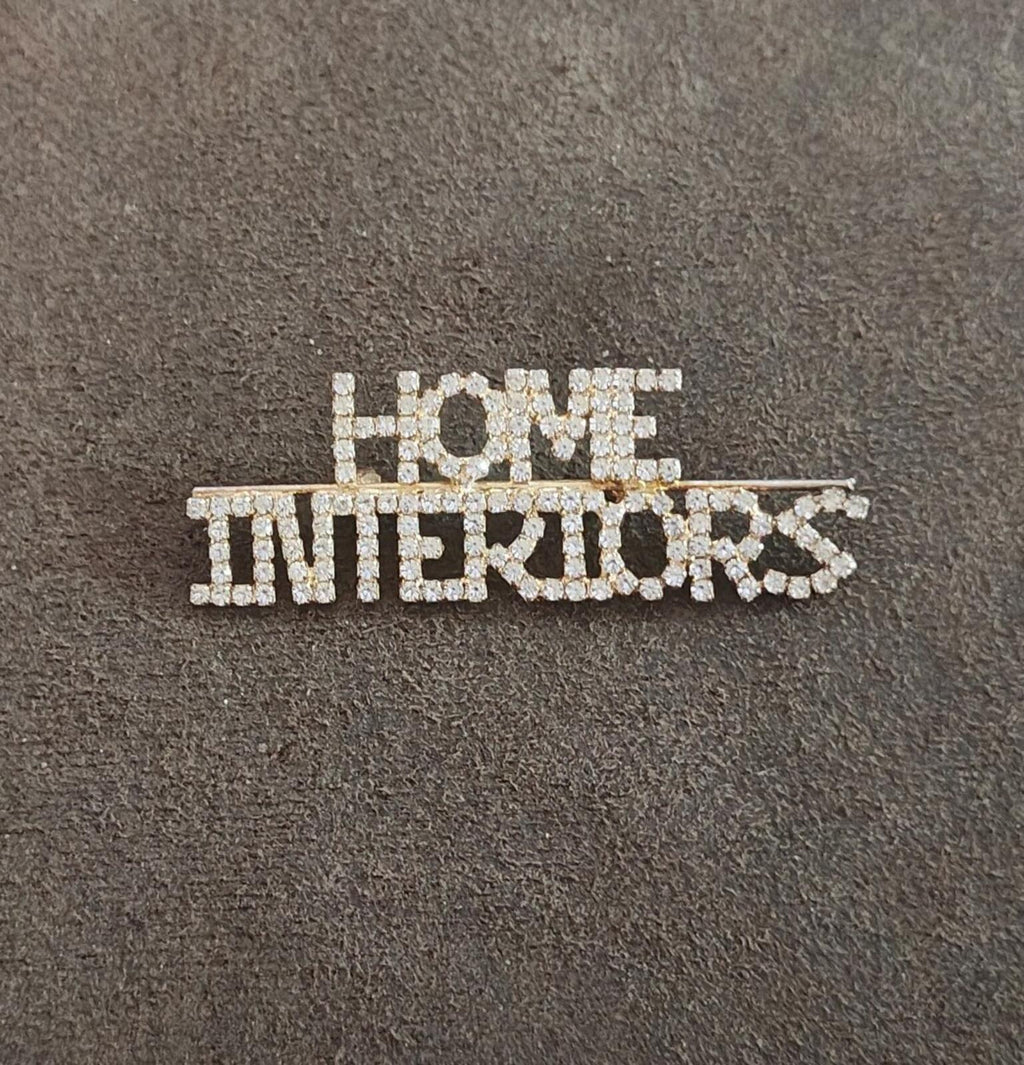 Rhinestone gold-tone brooch with "HOME" and "INTERIORS" lettering on a dark base