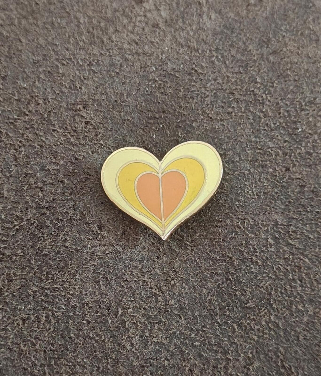 Yellow and orange enamel heart pin with gold tone edges on a dark surface.