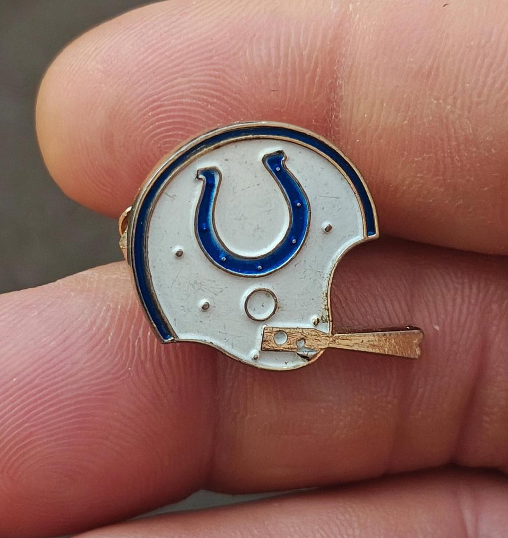 Gold-tone enamel tie clip close-up with white helmet and blue horseshoe on front