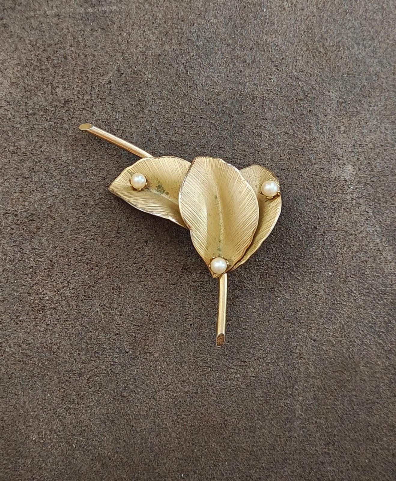Gold textured leaf brooch on a dark background with faux pearl accents