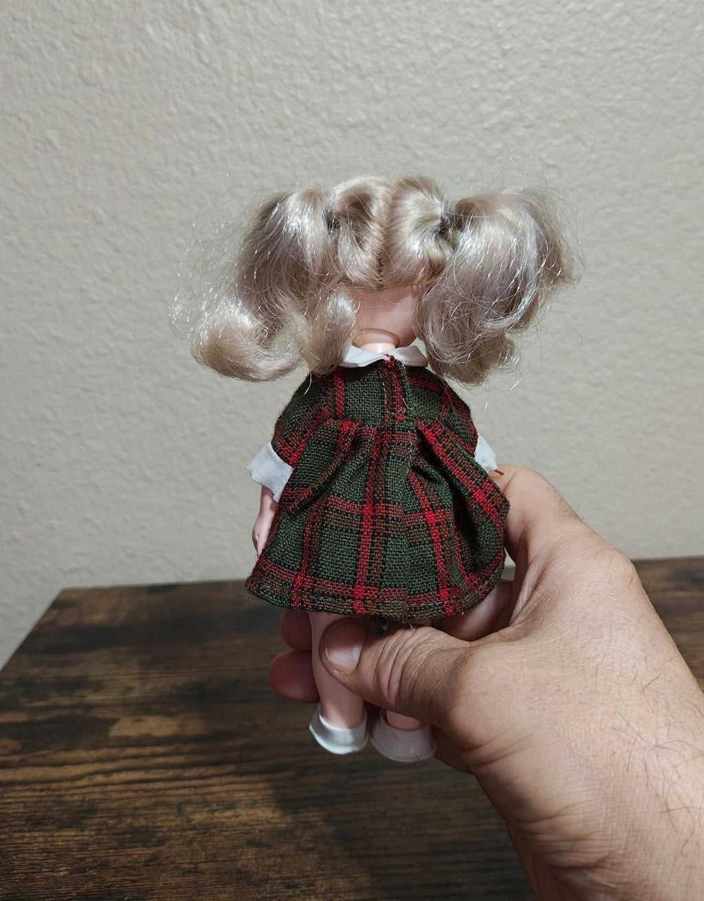 Vintage doll held from side view, green plaid dress and curly light-brown hair