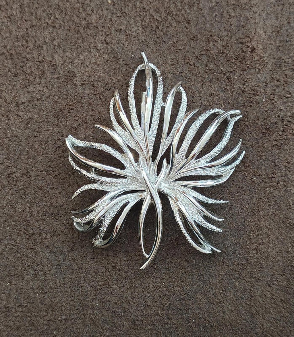 Silver tone leaf pin brooch with frosted texture, front view on flat surface