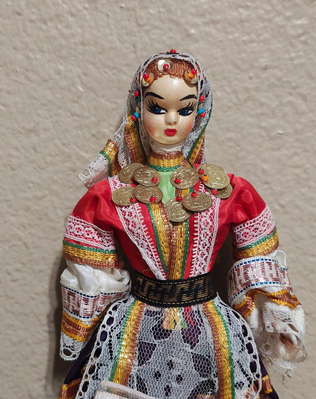 Female folk doll close-up with red dress, gold coin necklace, and jeweled headpiece