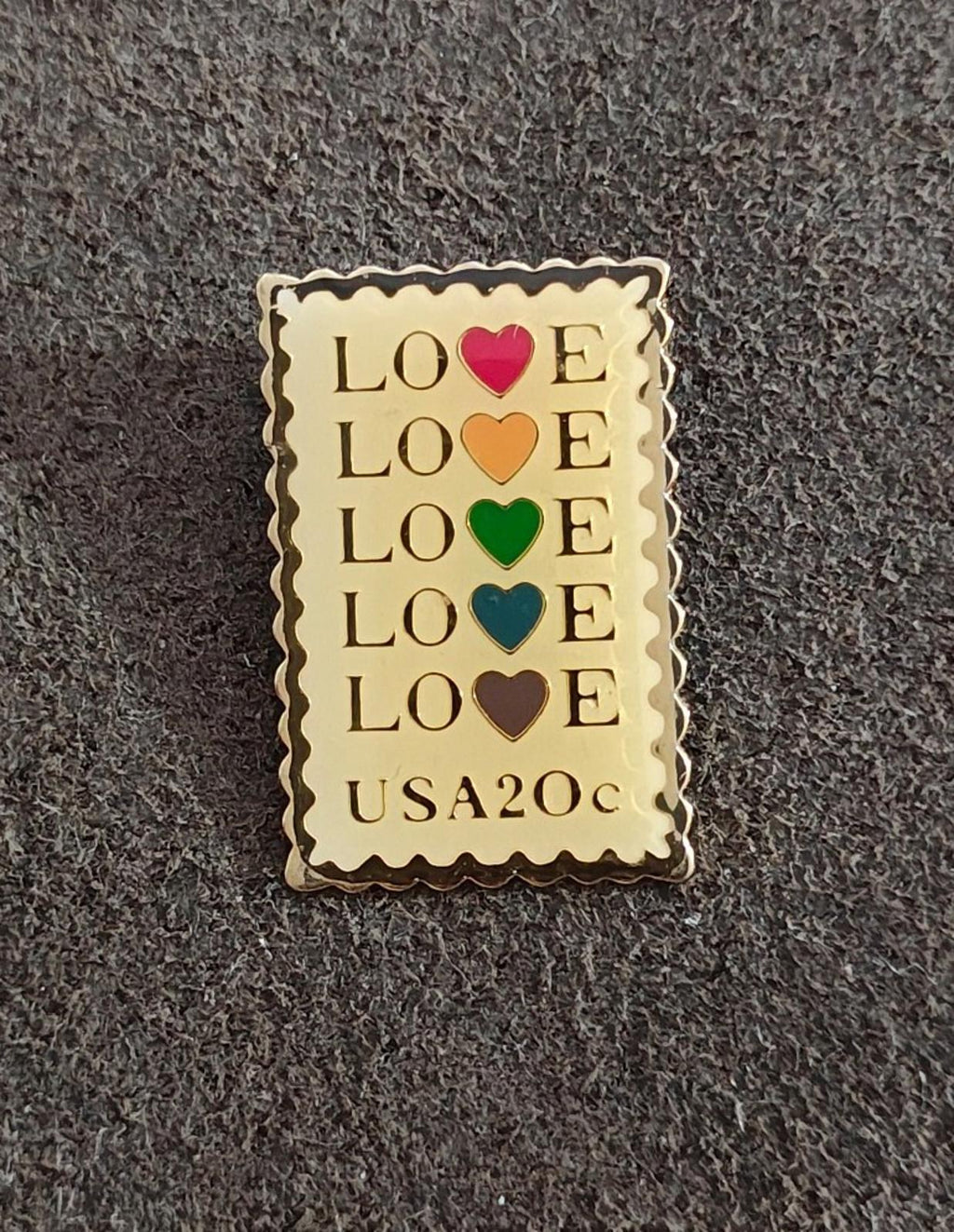 Gold-tone enamel rectangular pin with “LOVE” lettering and multicolor heart icons, “USA20c” text.
