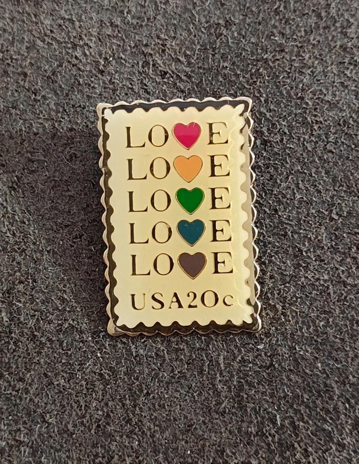 Gold-tone enamel rectangular pin with “LOVE” lettering and multicolor heart icons, “USA20c” text.